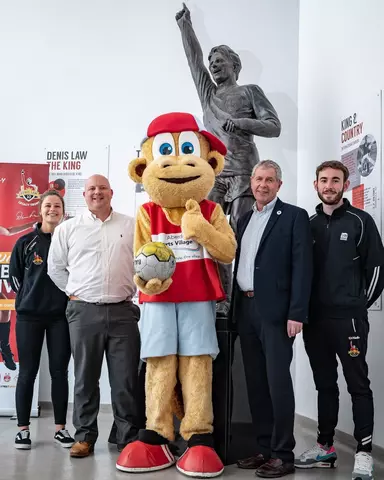 Mascot Asvil standing with sponsors and staff in front of the Denis Law statue at ASV.